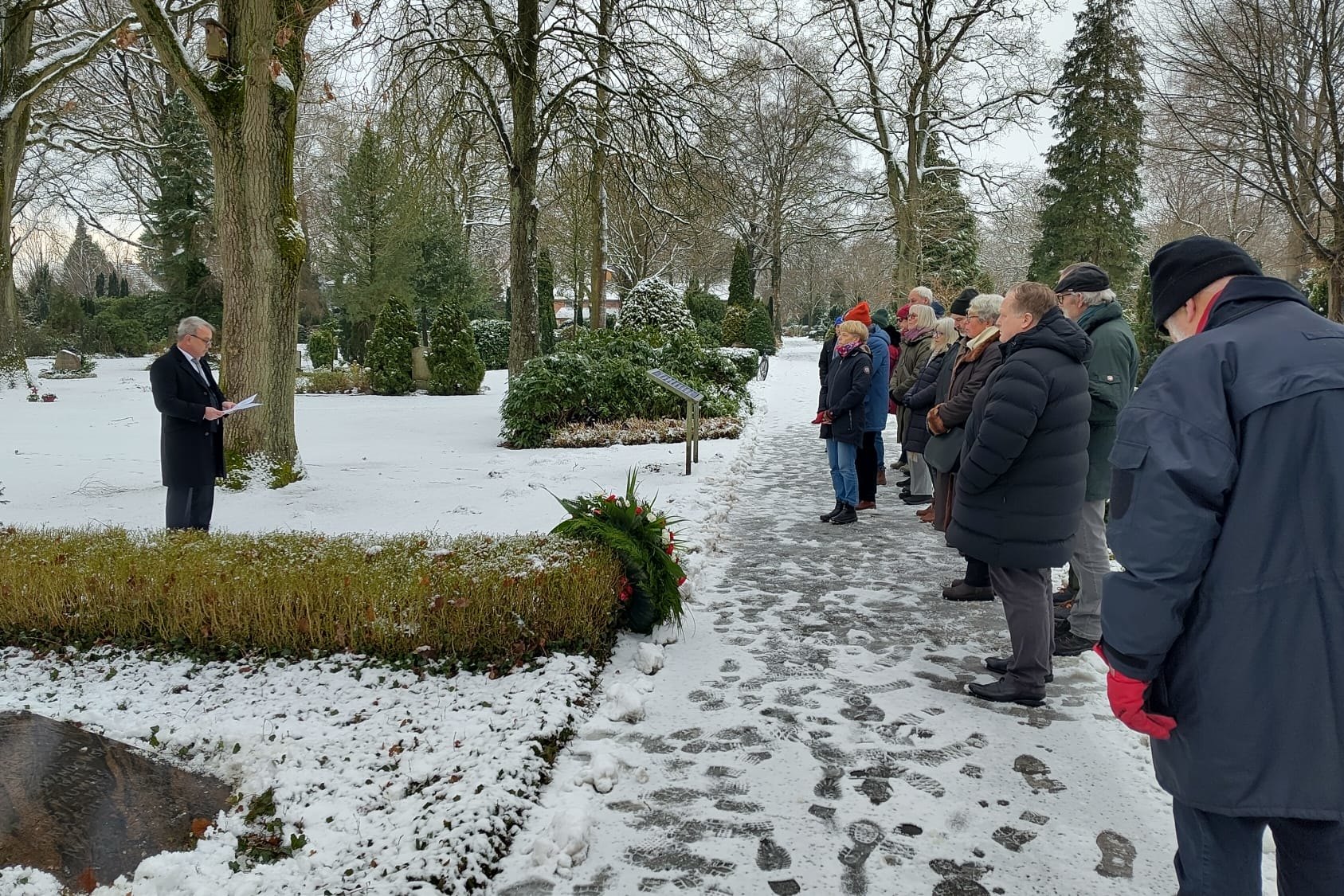 Cornelis de Jong hält die Ansprache auf dem verschneiten Barmstedter Friedhof, rechts stehen die Teilnehmenden der Gedenkveranstaltung