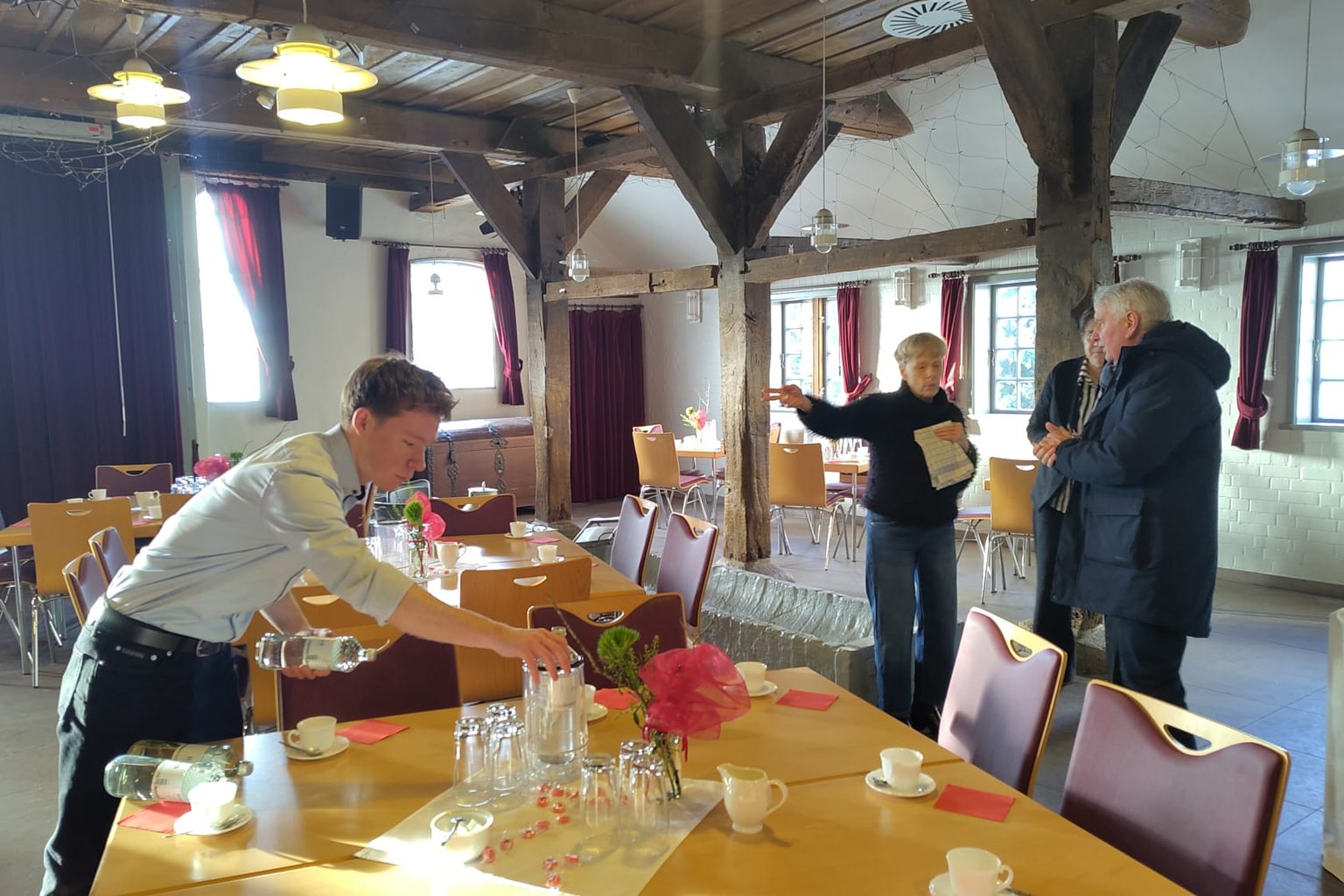Vorbereitungen im Humburg-Haus: Ein junger Mann deckt einen Tisch mit Wasserflaschen und Gläsern, im Hintergrund sprechen weitere Helfende